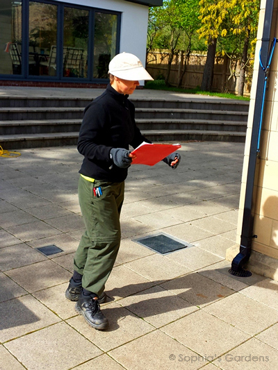 Sophia in work gear, clipboard in hand, surveying a garden