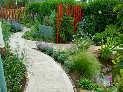 A garden designed to be adventurous yet have disabled access. The curved concrete path snakes through the garden, enclosing a pond, pole screens, flowerbeds and raised planters.